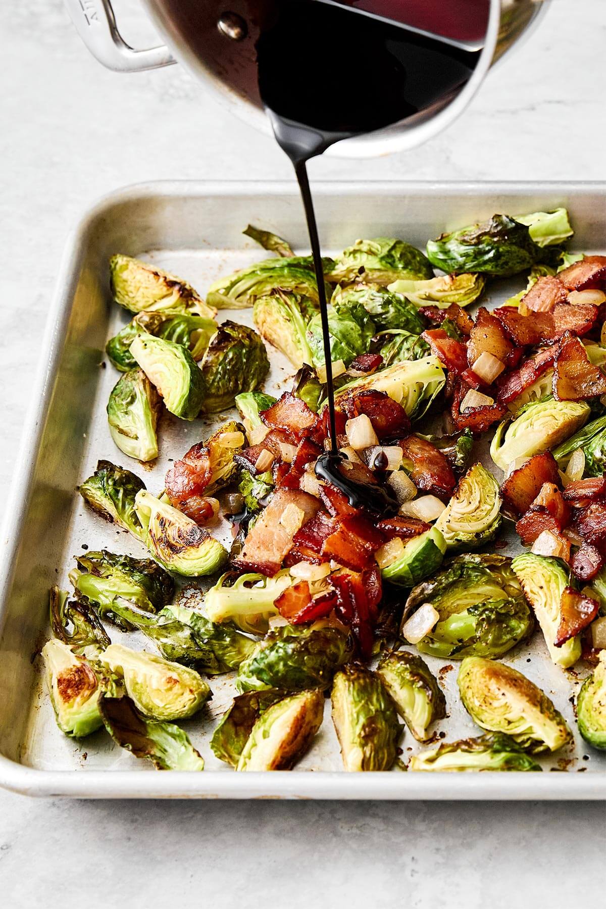 Pouring balsamic glaze over roasted Brussels sprouts.