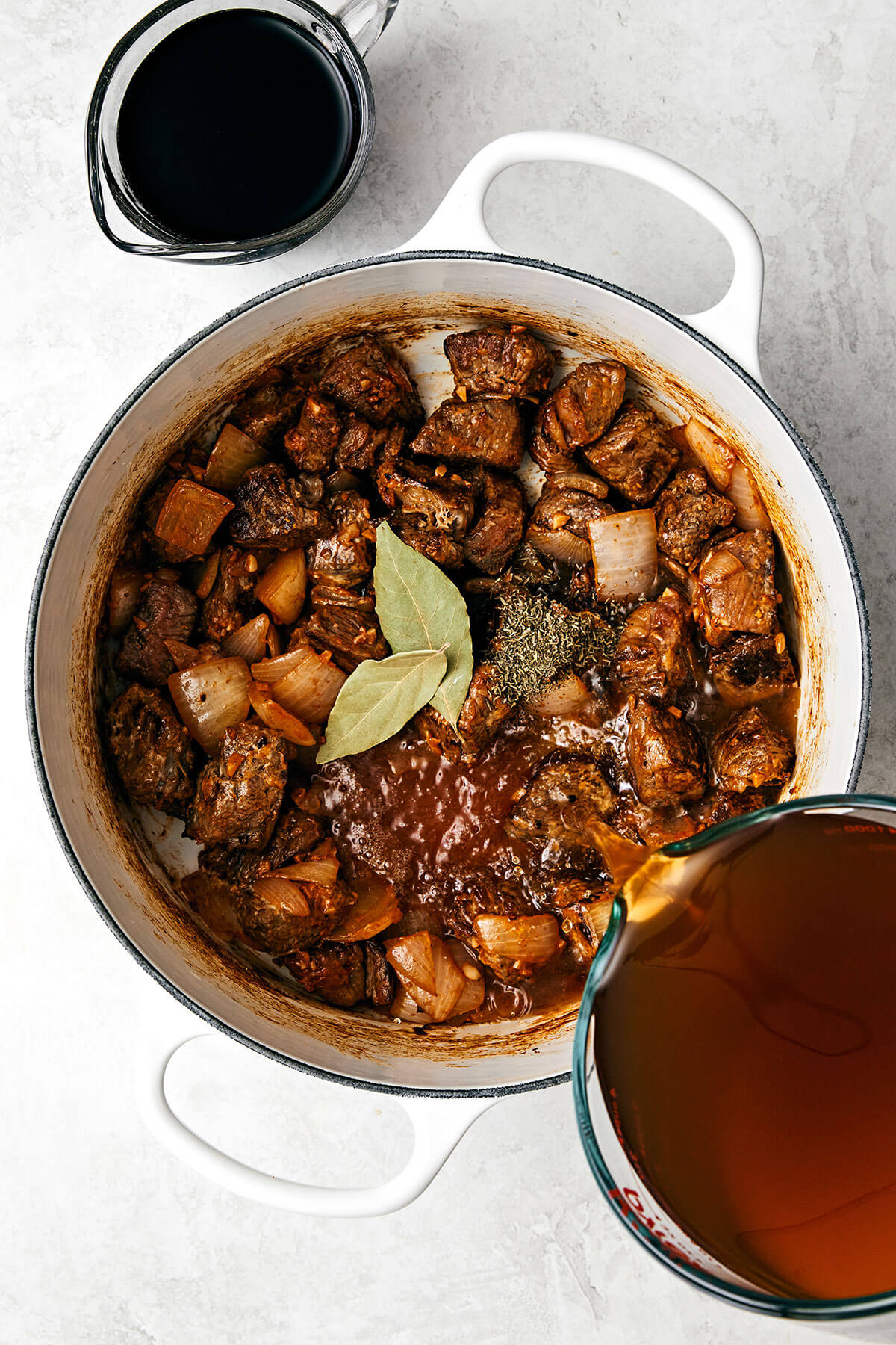 Pouring broth into a pot with beef stew meat