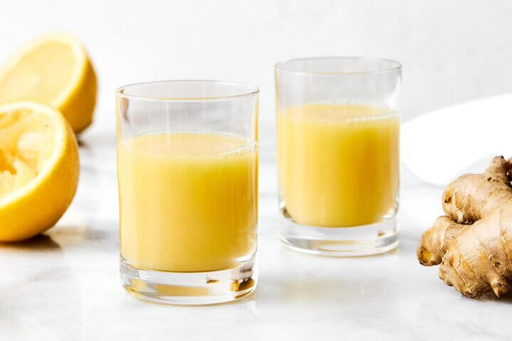 Cups of ginger shots next to lemons.