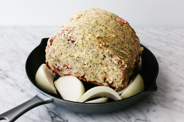 Prime rib with herb butter in a pan with onions.