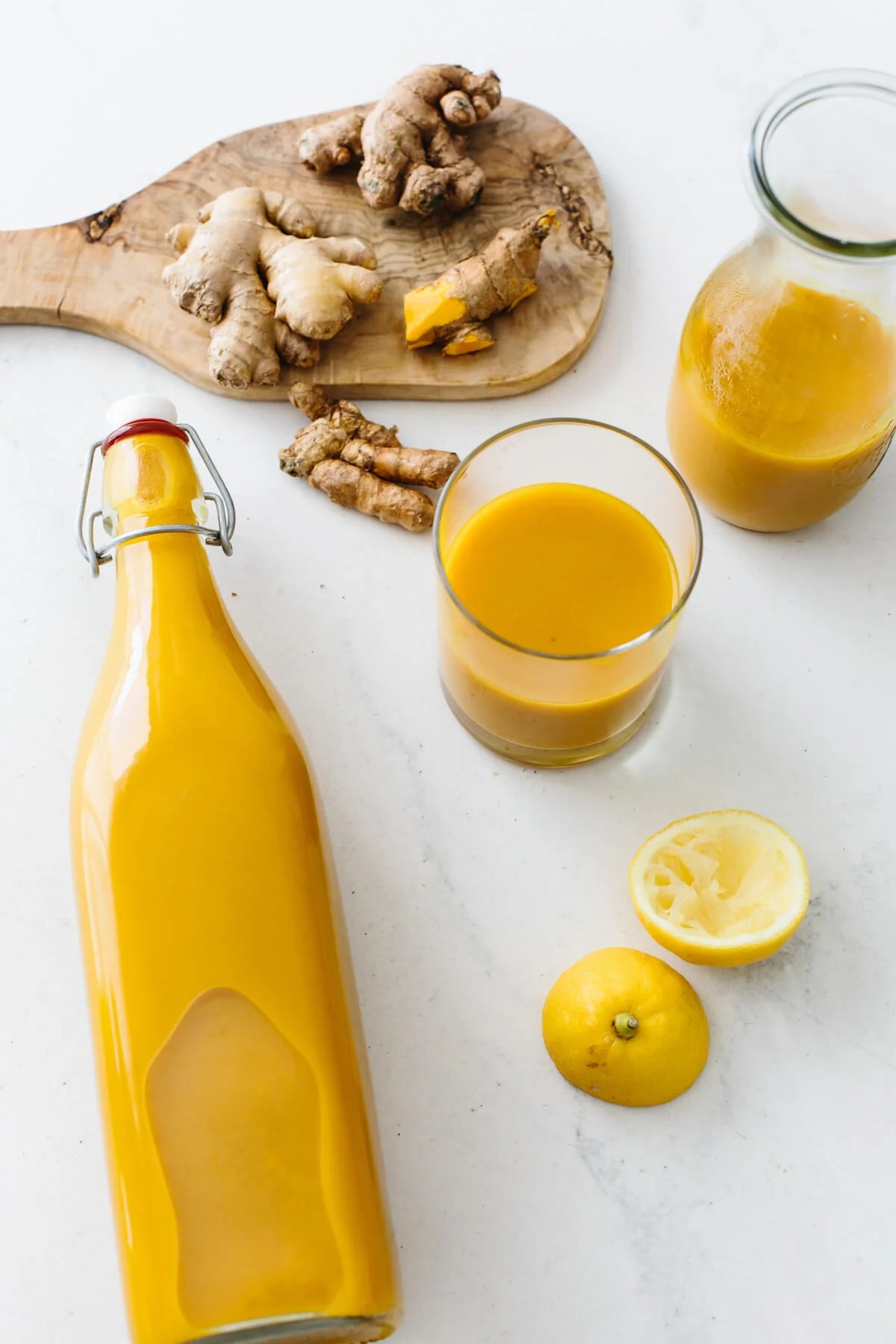 Jamu juice in a glass storage container next to turmeric and ginger.