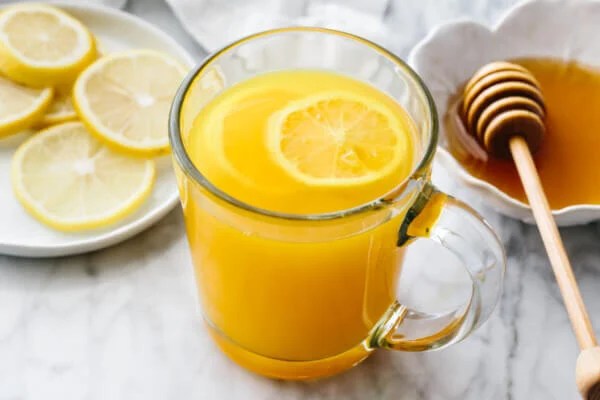 Turmeric tea in a glass with honey and lemon slices in the background.